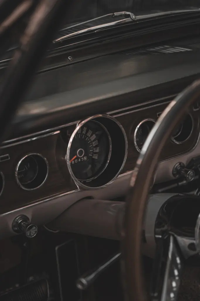 Detail palubní desky historického automobilu s tachometrem, volantem a chromovanými prvky interiéru.