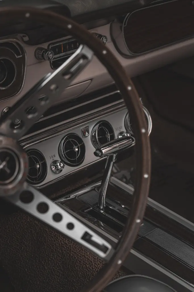 Detail interiéru historického automobilu s volantem, řadicí pákou a chromovanými prvky palubní desky.