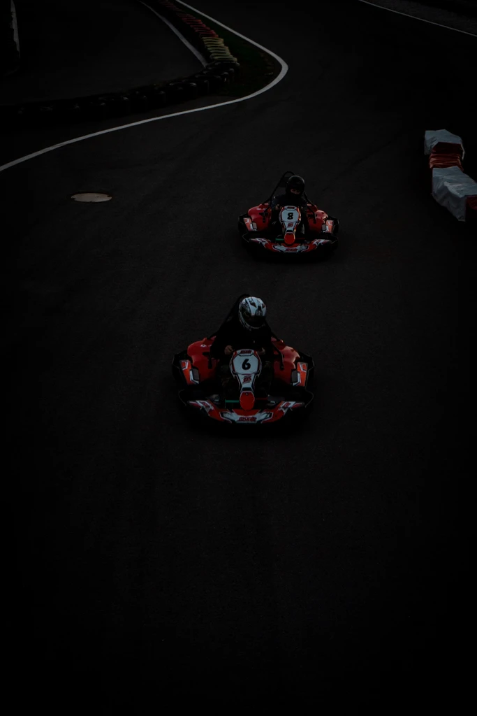 Dvě motokáry jedou po tmavé závodní trati během jízdy na venkovním okruhu.